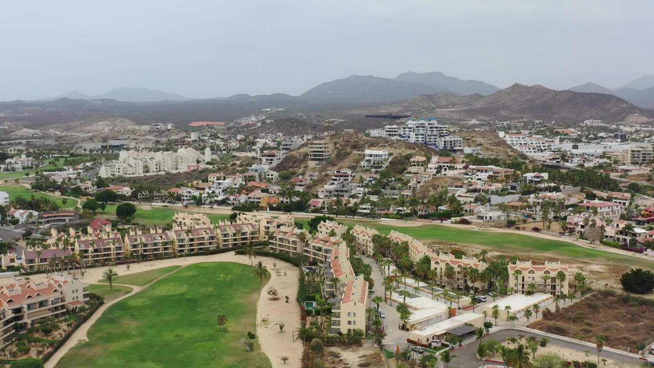 Aerial view of green grounds, apartment blocks, houses, and dry hills.