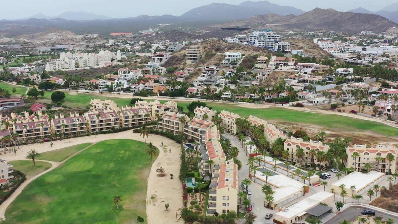 Aerial view of green fields, residential buildings, and dry hills.