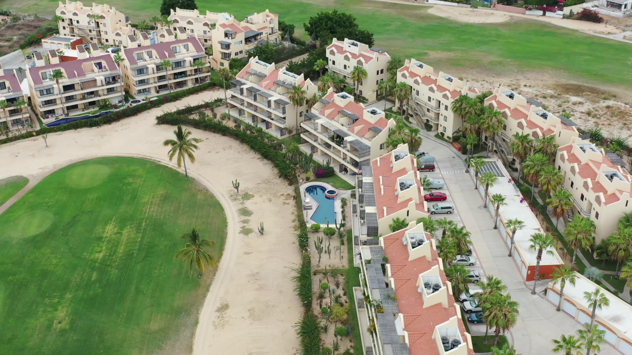 Aerial view of condominiums beside a green fairway and sandy paths.