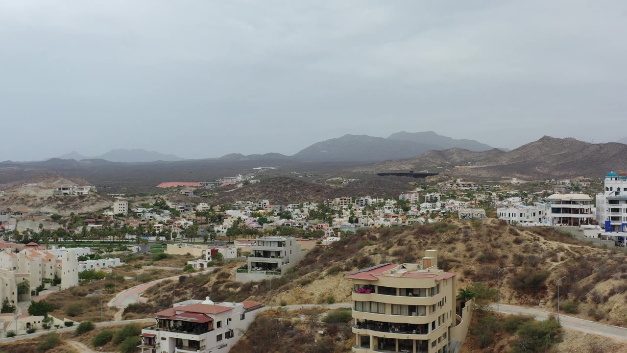 Second frame shows Los Cabos hillside housing and condo buildings spread across sandy terrain, with hazy mountains and no visible people.