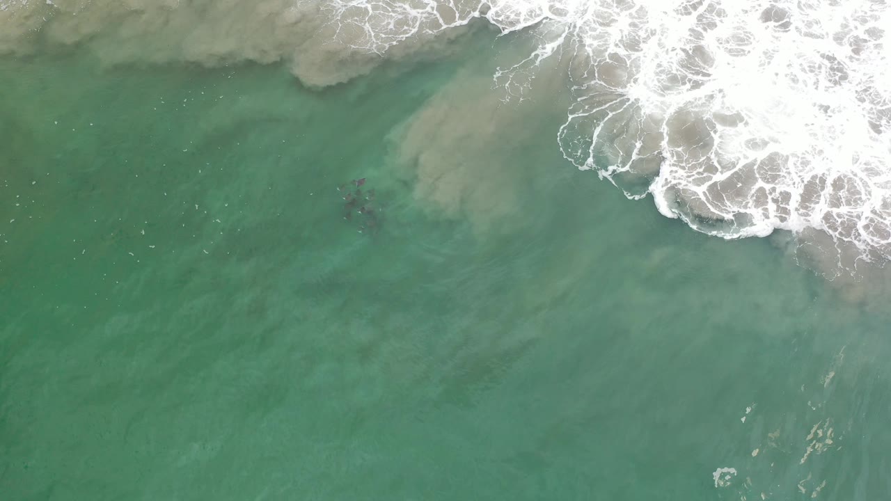 White surf curls over shallow green water with a dark underwater patch nearby.