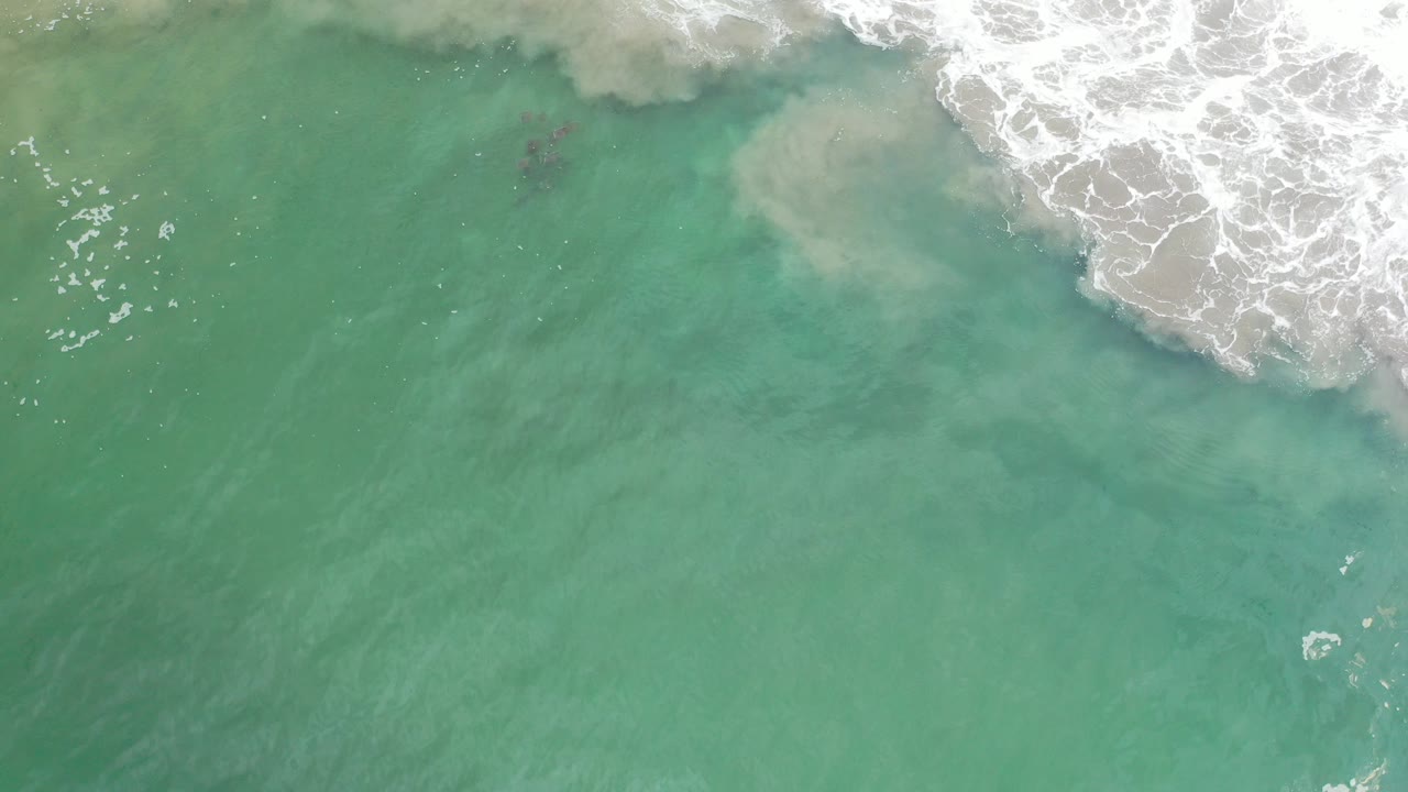 Top-down view of green seawater in Los Cabos, Mexico, with white surf entering from the upper right and no visible people.