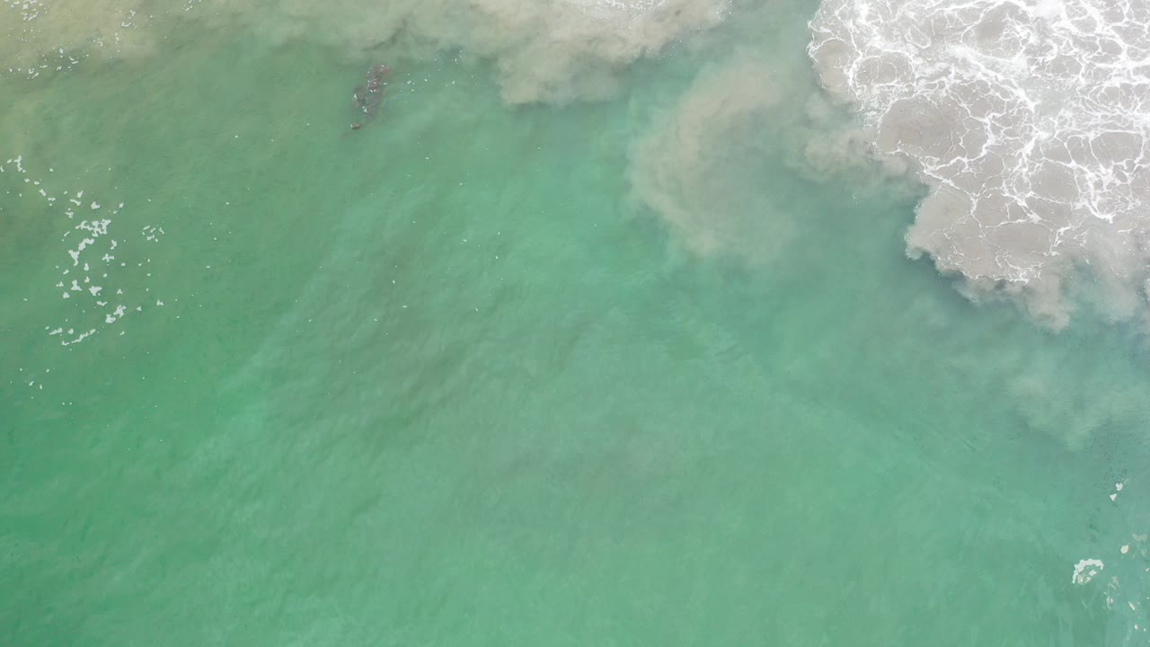 Overhead view of green-blue sea in Los Cabos, Mexico, with white surf entering from the top edge and no visible people.