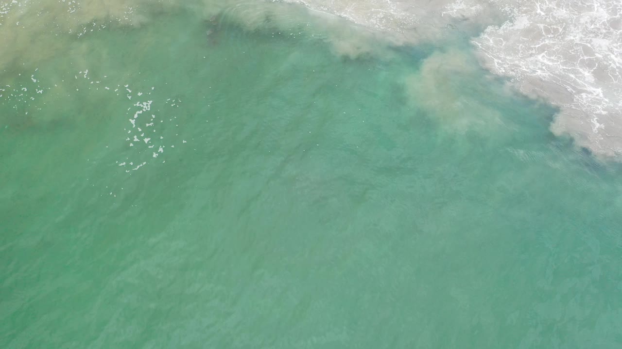 Aerial ocean surface with surf foam sliding across the upper right.