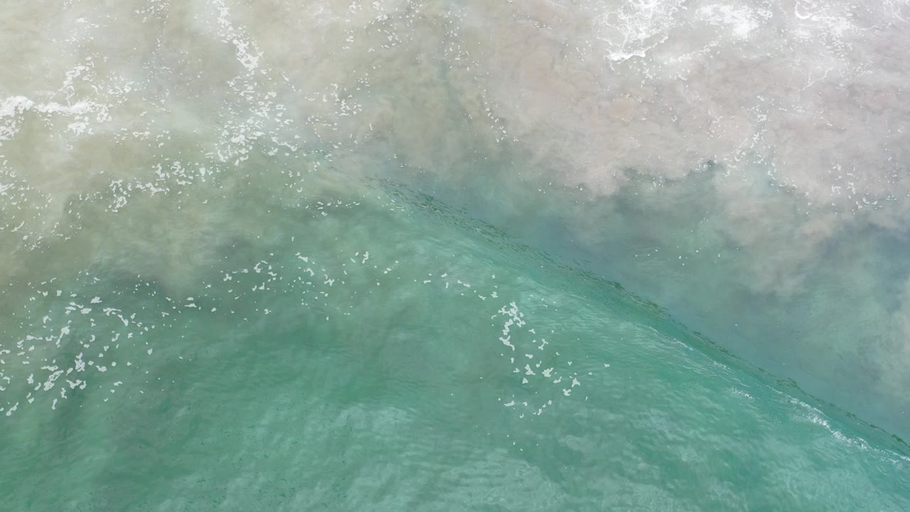 Overhead view in Los Cabos, Mexico, with turquoise water below pale wet sand and a thin band of white foam, no visible people.