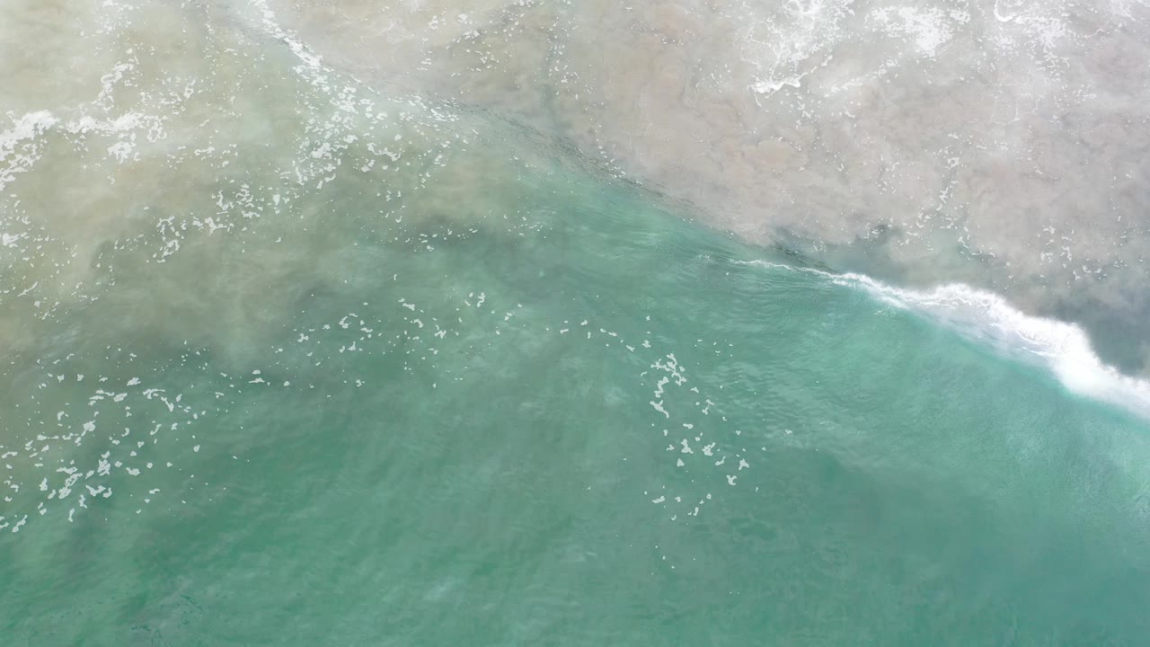 Foamy shorebreak rolling across green water.