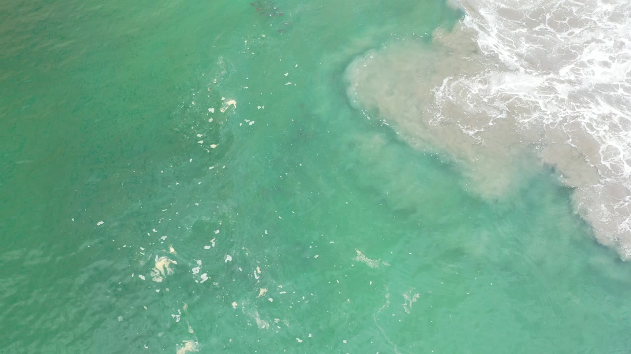 Overhead view of clear turquoise water in Los Cabos, Mexico, with pale surf foam entering from the upper right and no visible people.