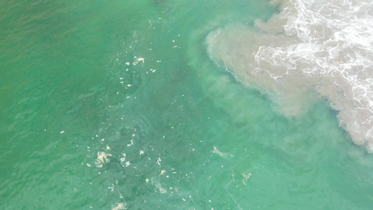 Aerial view of turquoise water with bright reflections and surf foam.