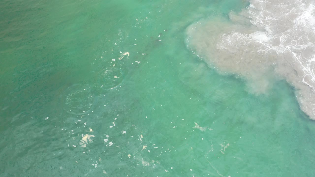 Overhead view of turquoise water and white surf washing across a pale sandbar in Los Cabos, Mexico, with no visible people.