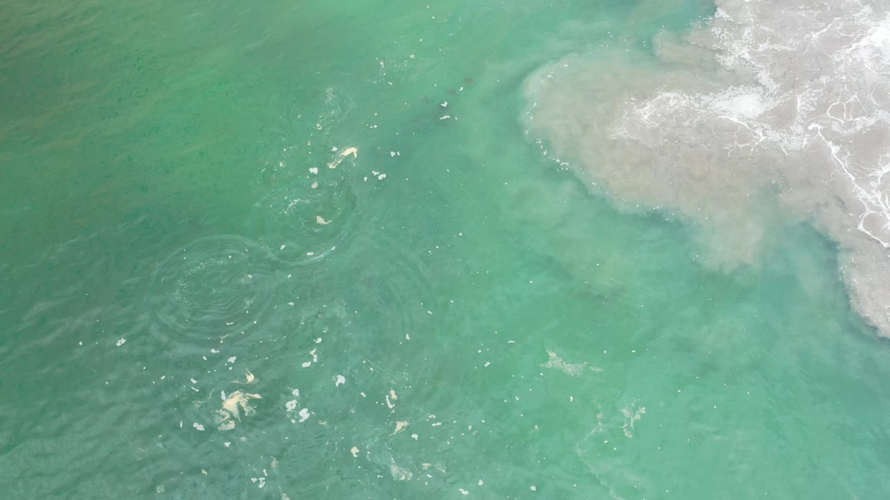 Overhead ocean texture with small sun reflections and white surf.