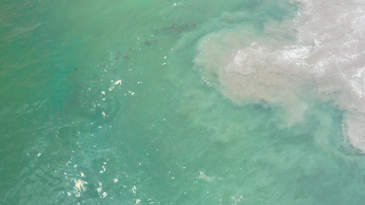 Turquoise ocean water with pale foamy sand wash near the upper right.
