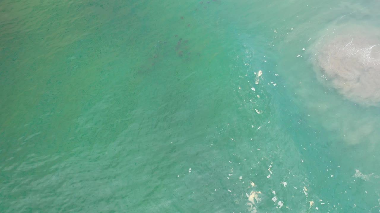 Turquoise water seen from above with a pale surf-like patch along the right edge.
