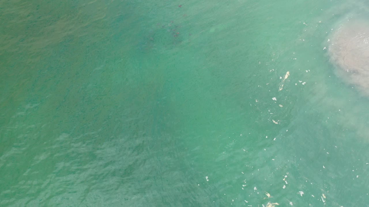 Overhead view of green ocean water in Los Cabos, Mexico, with a pale foamy patch near the upper right and no visible people.