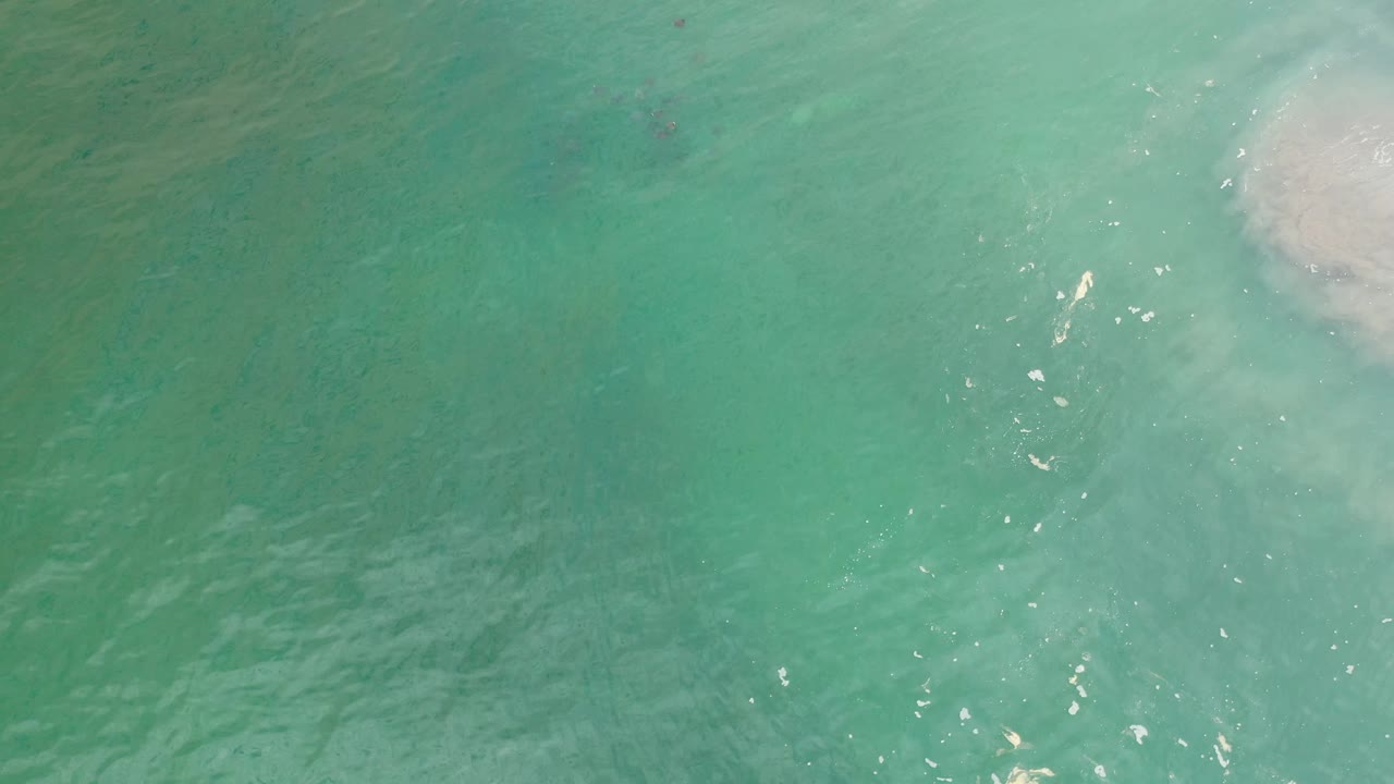 Turquoise-green ocean water fills the frame in Los Cabos, Mexico, with small bright reflections and a foamy wash near the right edge, no visible people.