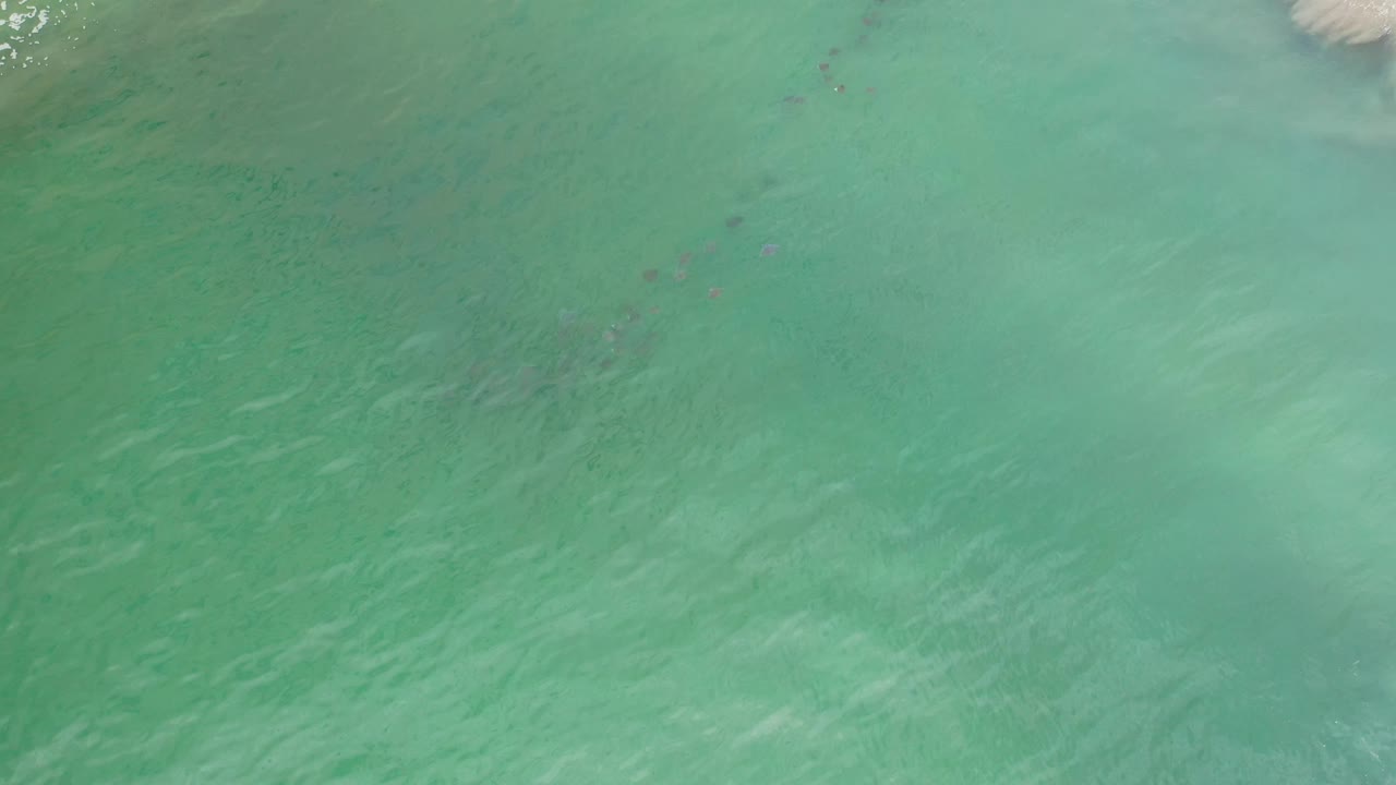 Aerial Los Cabos water frame showing turquoise-green sea, a pale foamy wave band near the top edge, and no visible people.