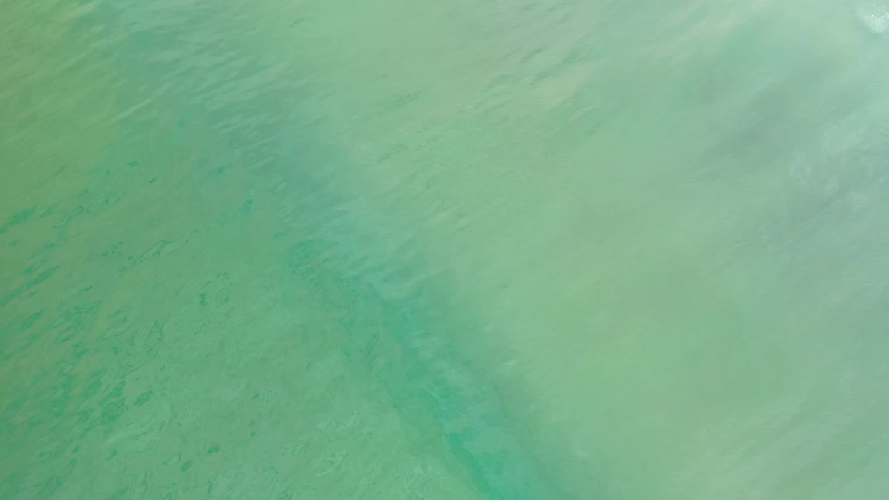 Aerial view of Los Cabos ocean water with darker underwater streaks and pale reflective patches, with no visible people.