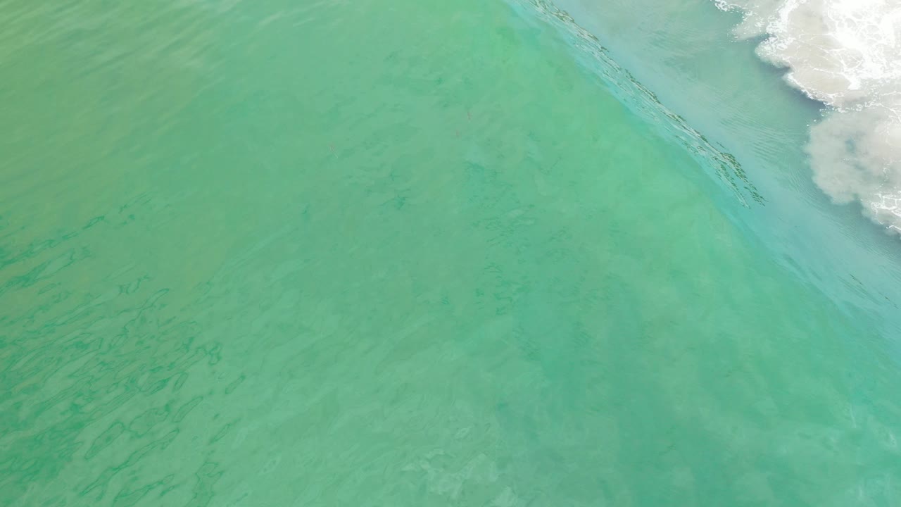 Overhead view of turquoise Los Cabos ocean water with a white surf line touching the upper edge and no visible people.
