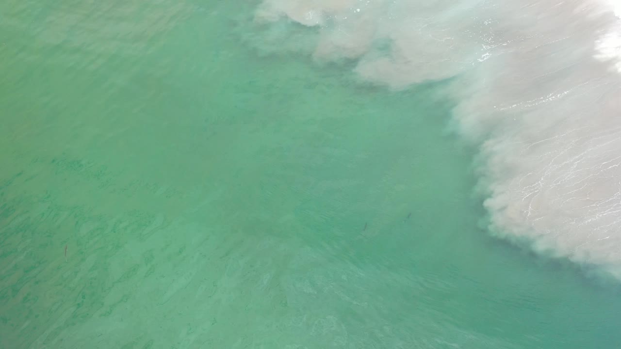 Green ocean surface with faint sand streaks and foam at the right side.