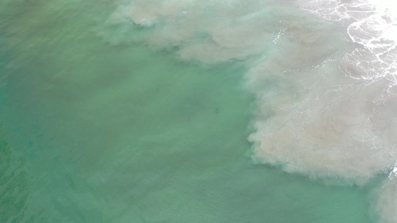 Overhead view of green ocean water and pale white surf foam in Los Cabos, Mexico, with no visible people at the start of the clip.