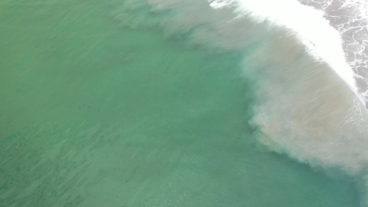 High overhead view of green ocean water in Los Cabos, Mexico, with a white breaking wave entering from the top right and no visible people.