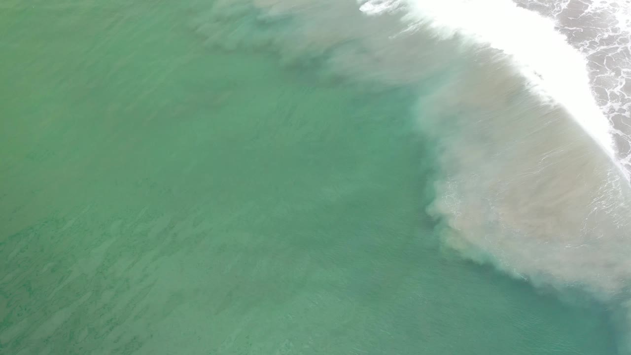Overhead Los Cabos ocean frame with green water, a pale foam cloud near the right side, and no visible people or vessels.
