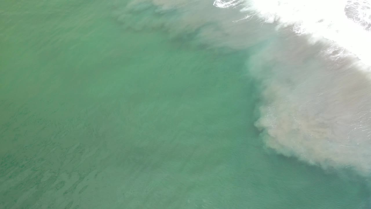 Aerial view of green surf water with foamy white wash along the upper right.
