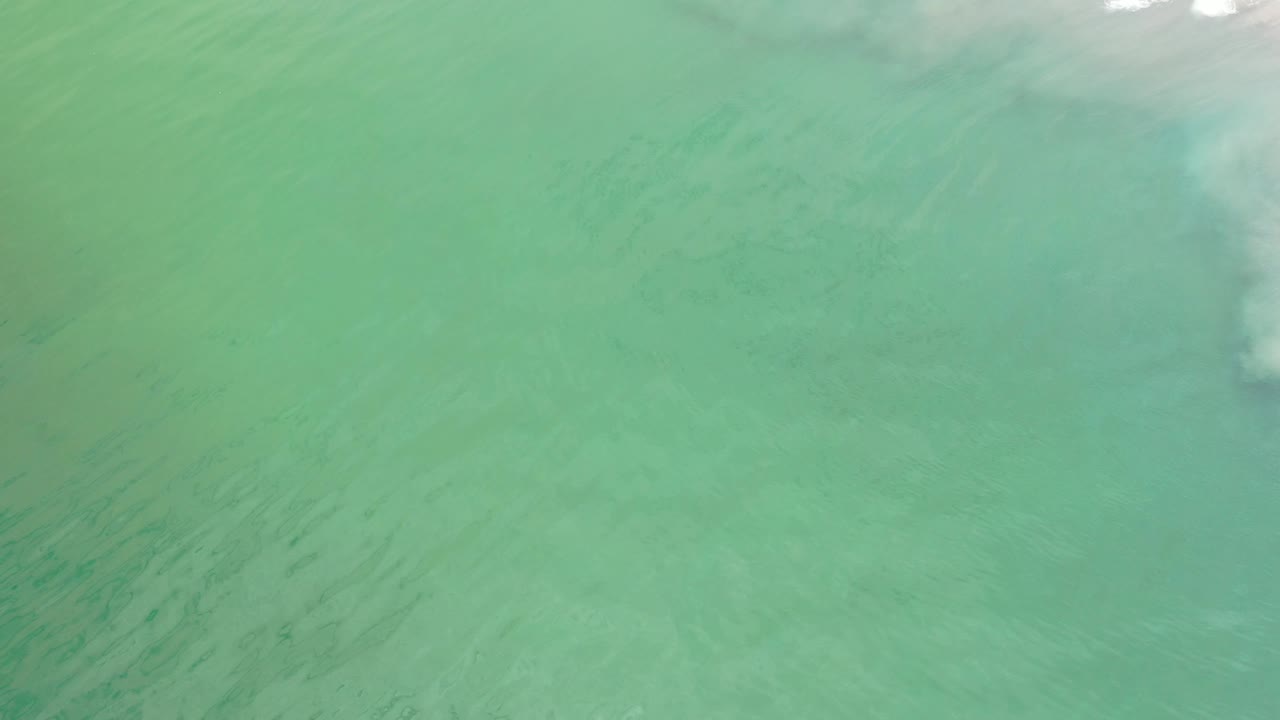 Wide field of pale green water with subtle darker ripple patterns.