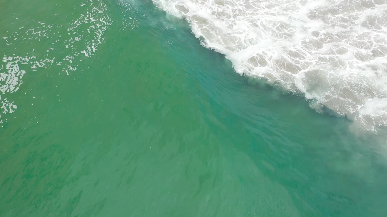 Foamy surf curls over green ocean water from the upper right.