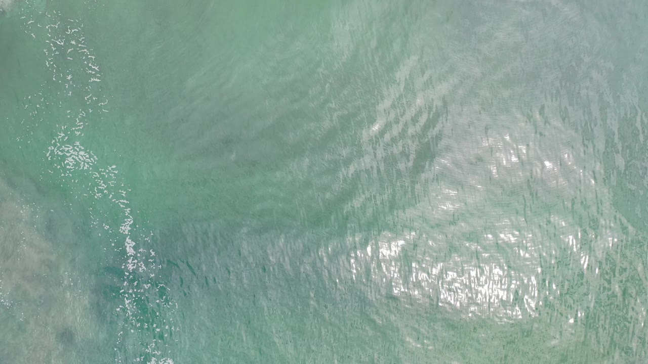 Top-down view of turquoise ocean water in Los Cabos, Mexico, with rippled surface texture, bright sun reflection, and no visible people.
