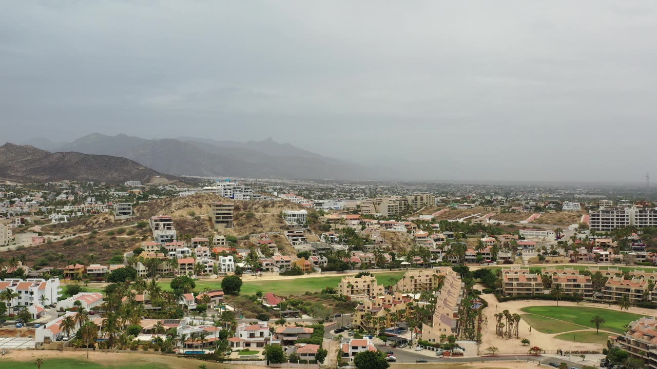 Los Cabos aerial view with green grounds, roads, buildings, and overcast haze.