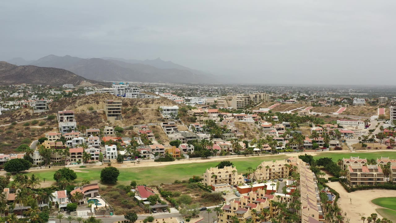 Residential neighborhood and green strip below brown hills and hazy sky.