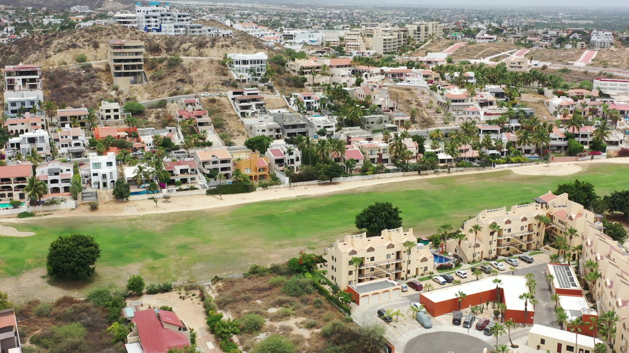 Aerial view of grass field beside low-rise homes and hillside buildings.