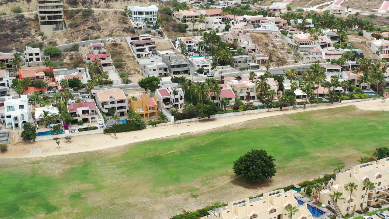 Aerial view of villas, road, sandy strip, and green open space.