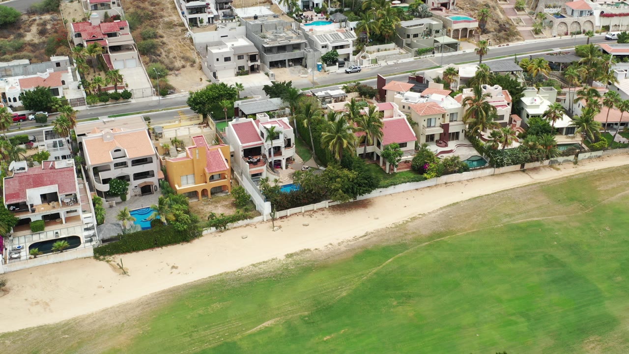 Aerial view of beachfront houses, road, sand, and green water.