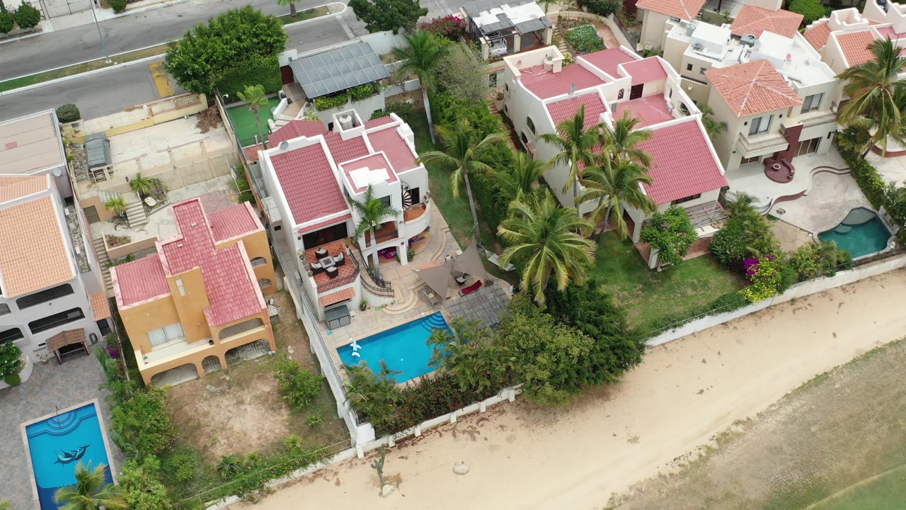 Overhead view of pink-roofed homes, pools, palms, and a road.