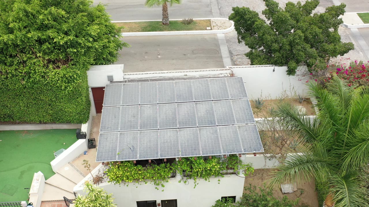 Aerial view in Los Cabos, Mexico, holding on the rectangular metal canopy over a white building entrance, with hedges and a road visible above and no visible people.