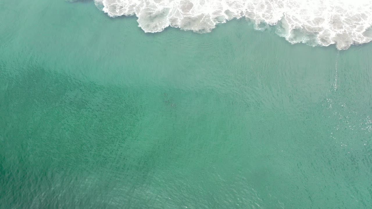Overhead view of turquoise green water in Los Cabos, Mexico, with white surf breaking across the top edge and no visible people.