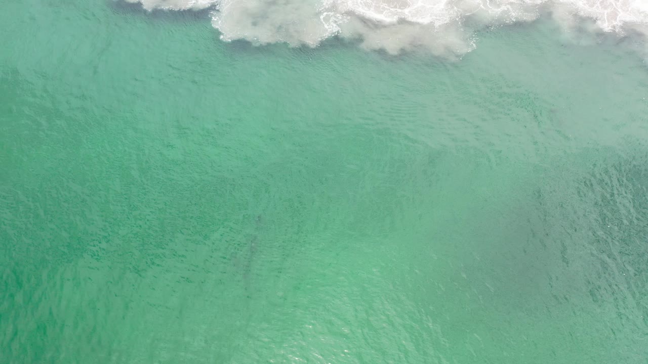 Overhead view of emerald ocean water in Los Cabos, Mexico, with white surf crossing the top edge and no visible people.