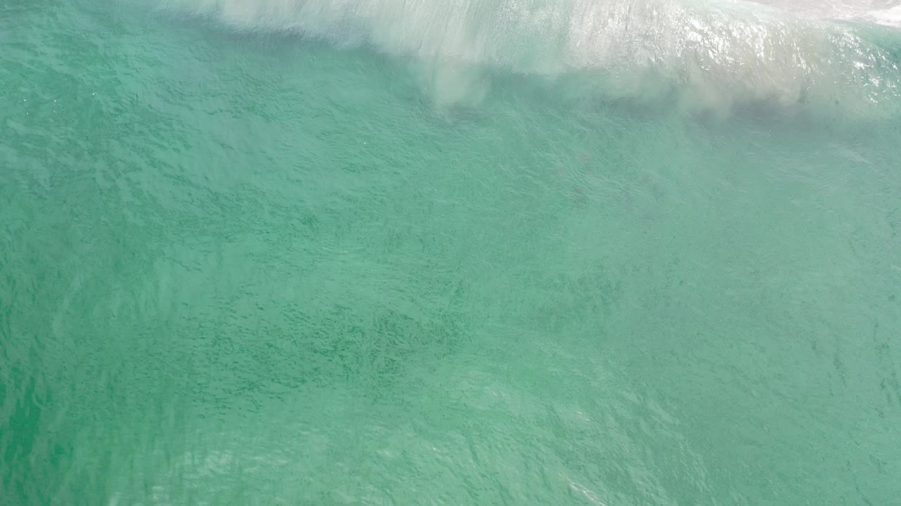 Overhead view of turquoise ocean water in Los Cabos, Mexico, with white surf foam along the upper edge and no visible people.