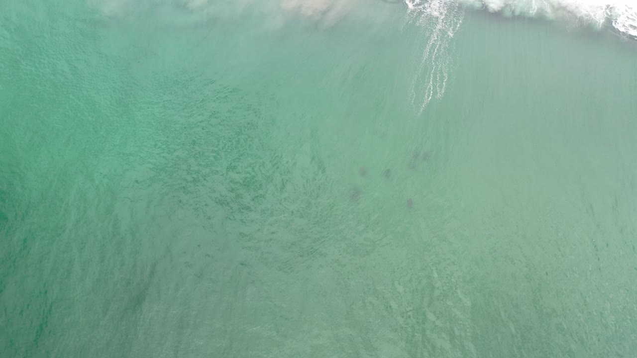 Overhead turquoise ocean water in Los Cabos, Mexico, with a thin strip of white surf entering along the upper edge and no visible people.