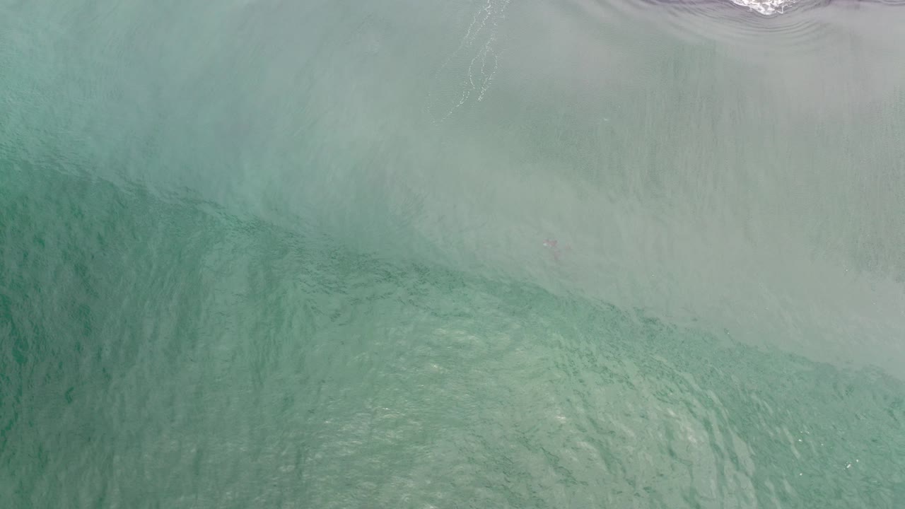 Overhead view of blue green water spreading over pale sand in Los Cabos, Mexico, with a thin foam line near the top and no visible people.