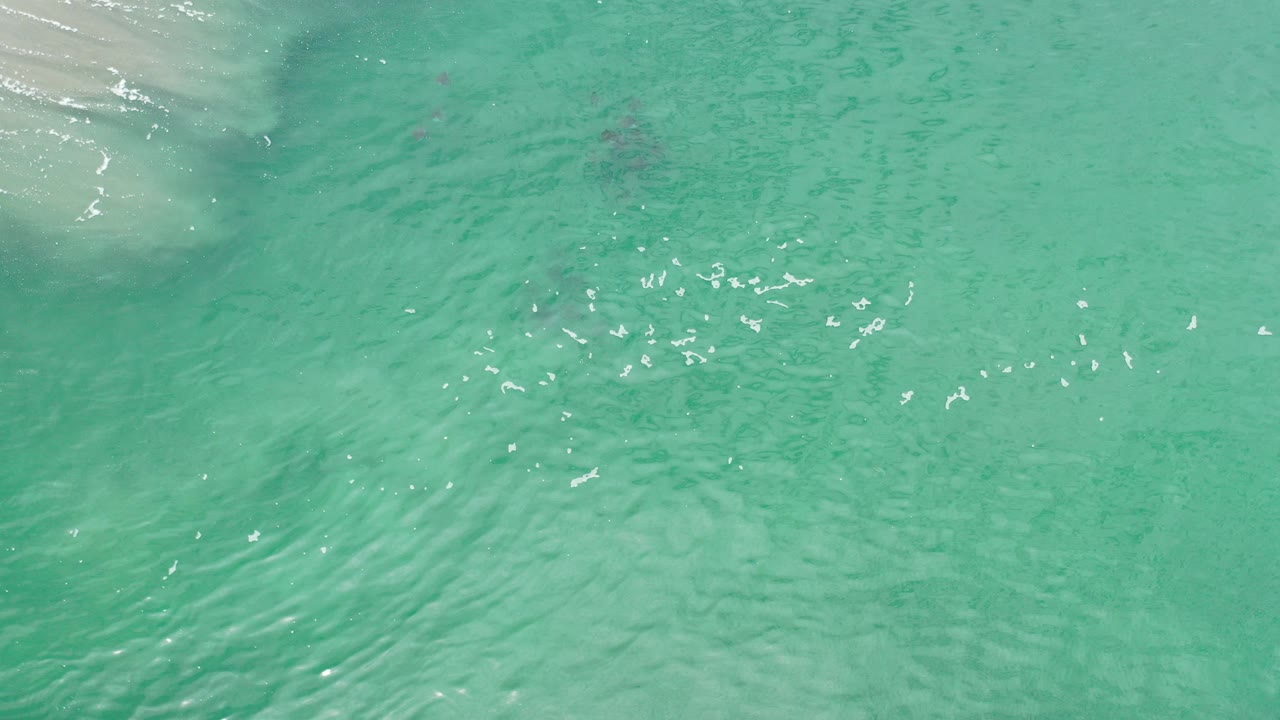 Overhead view of green-turquoise water in Los Cabos, Mexico, with faint rocks below the surface, bright ripple highlights, and no visible people.