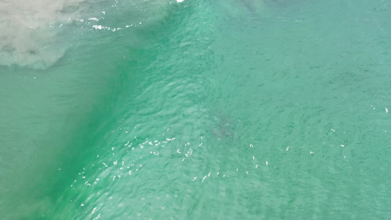Turquoise Los Cabos shoreline water shows a thin white wave edge across the top, faint sandy bottom below, and no visible people.