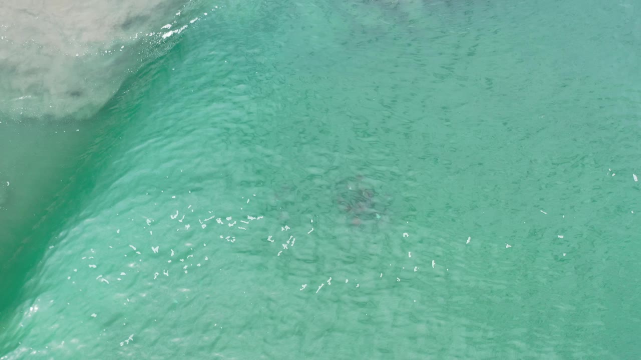 Curved green wave face over shallow sandy water.