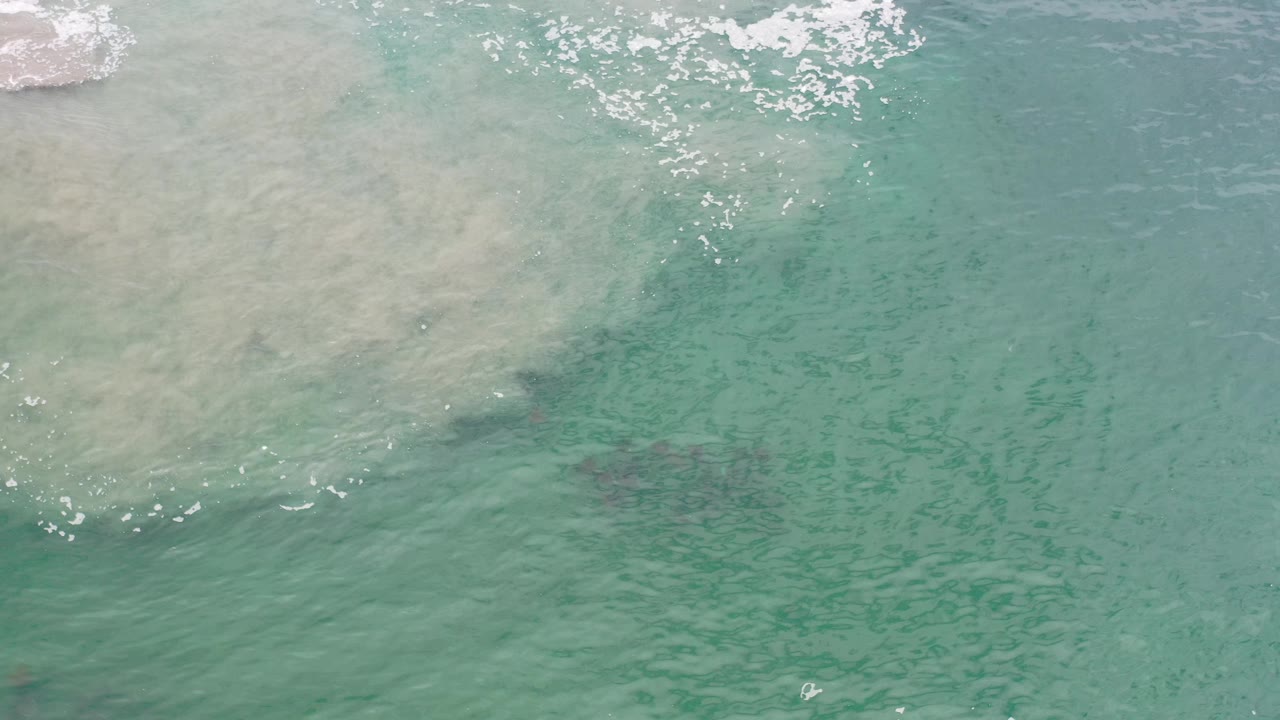 Aerial view of shallow turquoise water with darker patches beneath the surface.