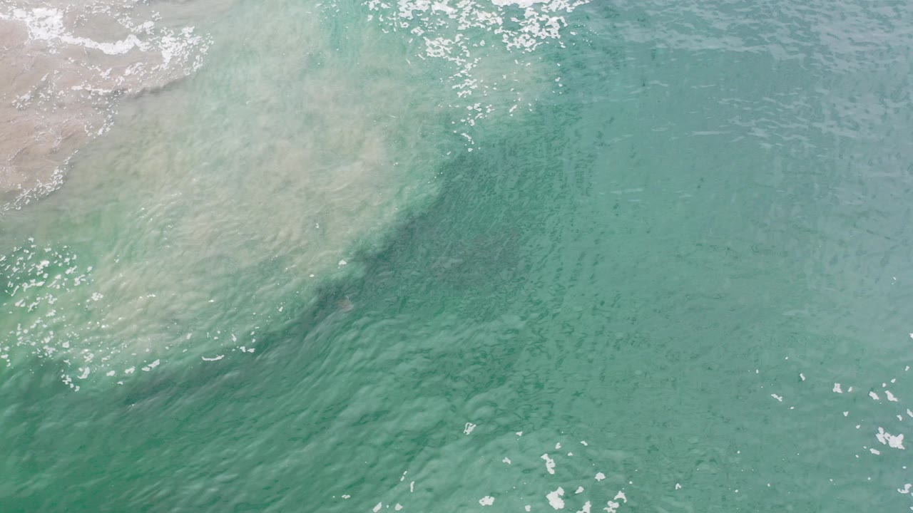 Overhead turquoise ocean water with pale sand clouding at the upper left.
