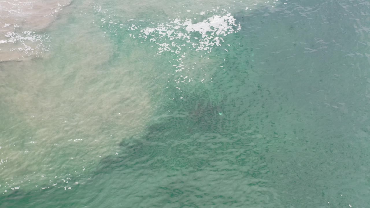 Aerial-style view of shallow turquoise surf with white foam and ripples.