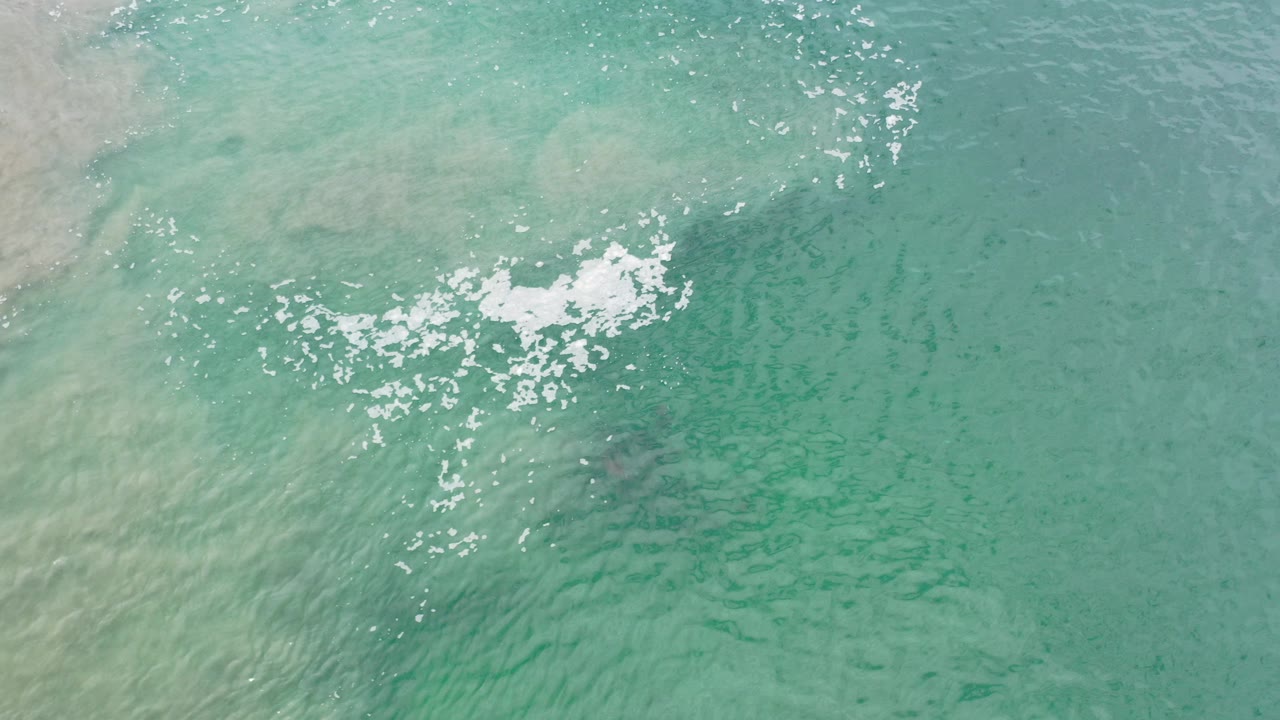 Overhead view of blue-green Los Cabos ocean water with a bright whitecap cluster, pale sandy mixing at left, and no visible people.