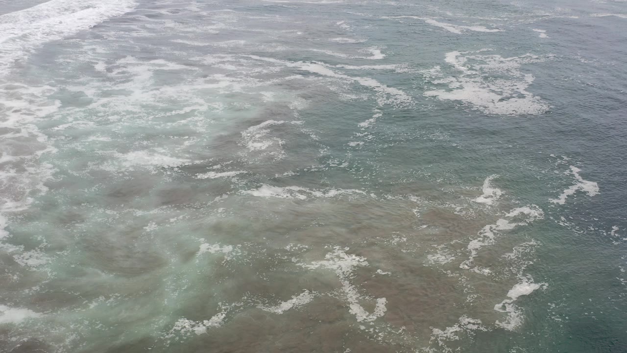 Opening aerial frame over rough teal and green ocean water in Los Cabos, Mexico, with white foam streaks across the surface and no visible people.
