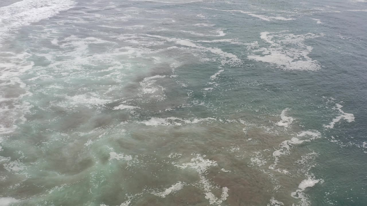 Overhead ocean water with dense foam and pale green swirls.